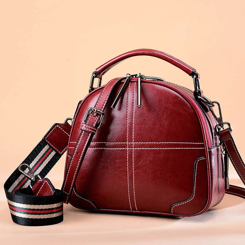 Round leather handbag with double soft handles and a zipper, shown in wine red colour.