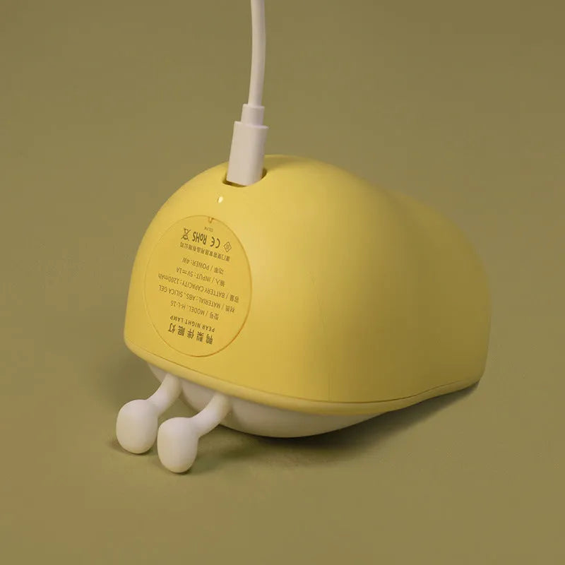 PEAR warm yellow silicone bedside night light with ABS base on a table.