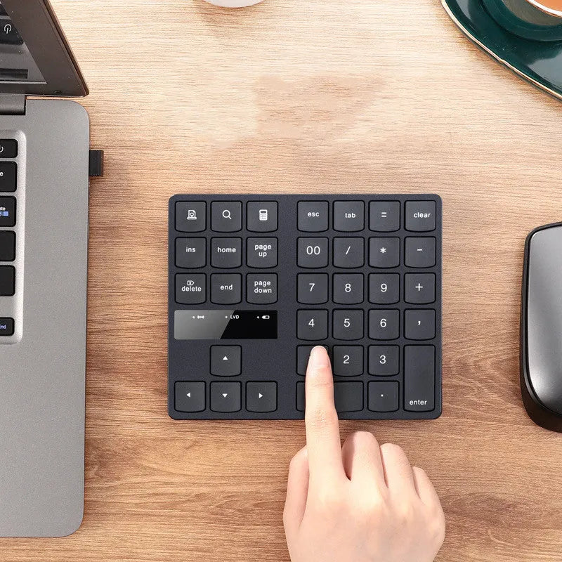 Black 35-key wireless numeric keyboard on desk with USB receiver and charging cable