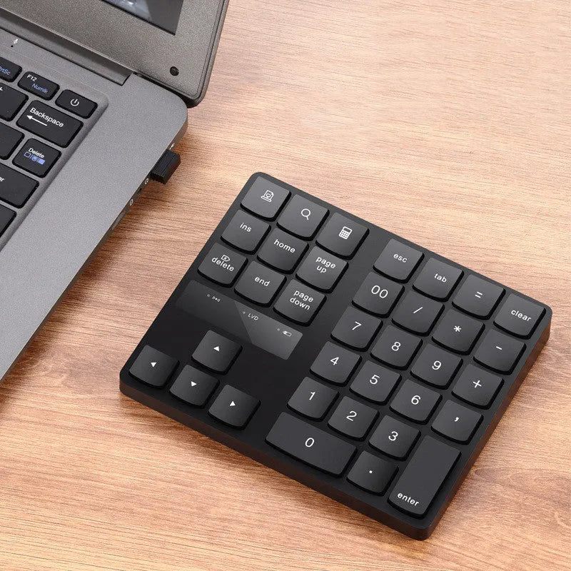 Black 35-key wireless numeric keyboard on desk with USB receiver and charging cable