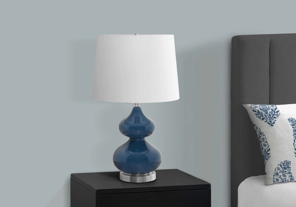 Blue crystal glass desk lamp with white fabric shade on a wooden desk.