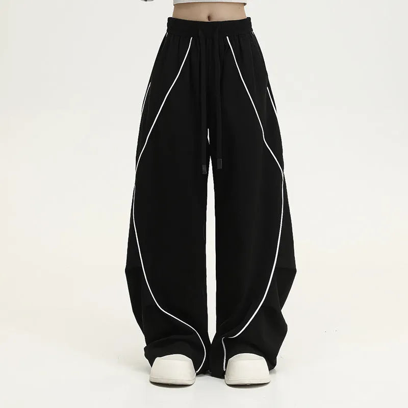 Black trousers with vertical stripes and pleated detail on the legs, showing a loose wide-leg fit.