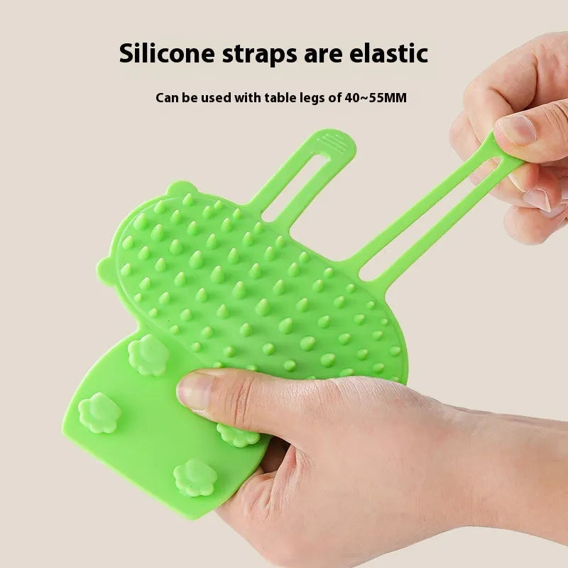 Black silicone cat grooming comb with rounded teeth and adjustable mounting strap for table legs.