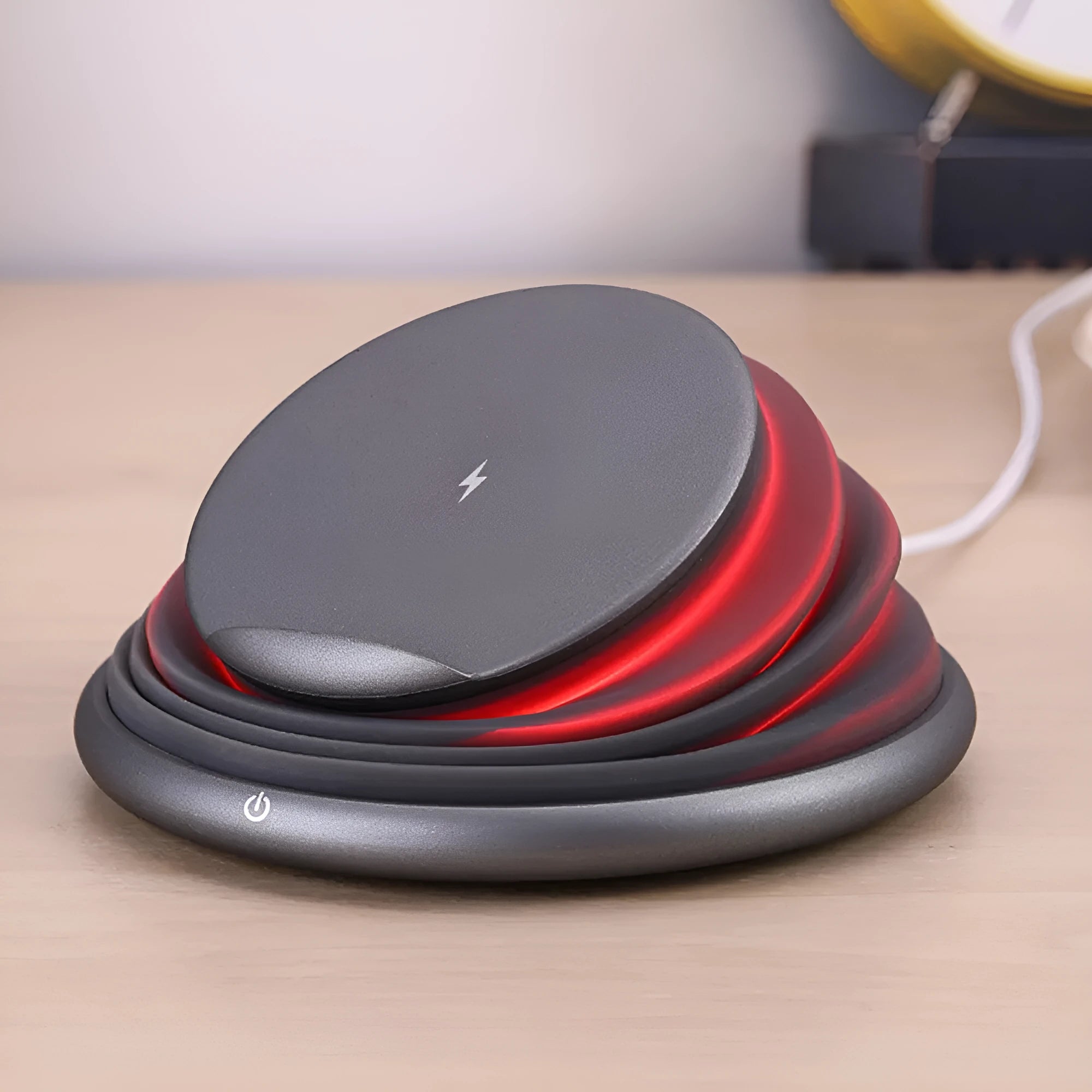 Grey wireless charging pad on a desk, 138x138x30mm, with silicone top surface and LED indicator