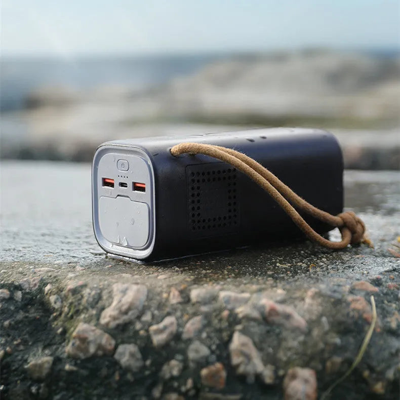 Black portable power bank with digital display, 220V socket, and USB ports on a wooden table.