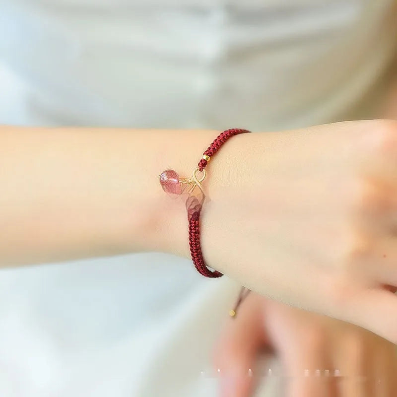 Women's bracelet with a natural strawberry quartz cherry charm on a black elasticated string.