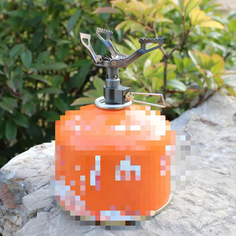 Portable metal propane camping stove with one-piece furnace design on a outdoor surface.