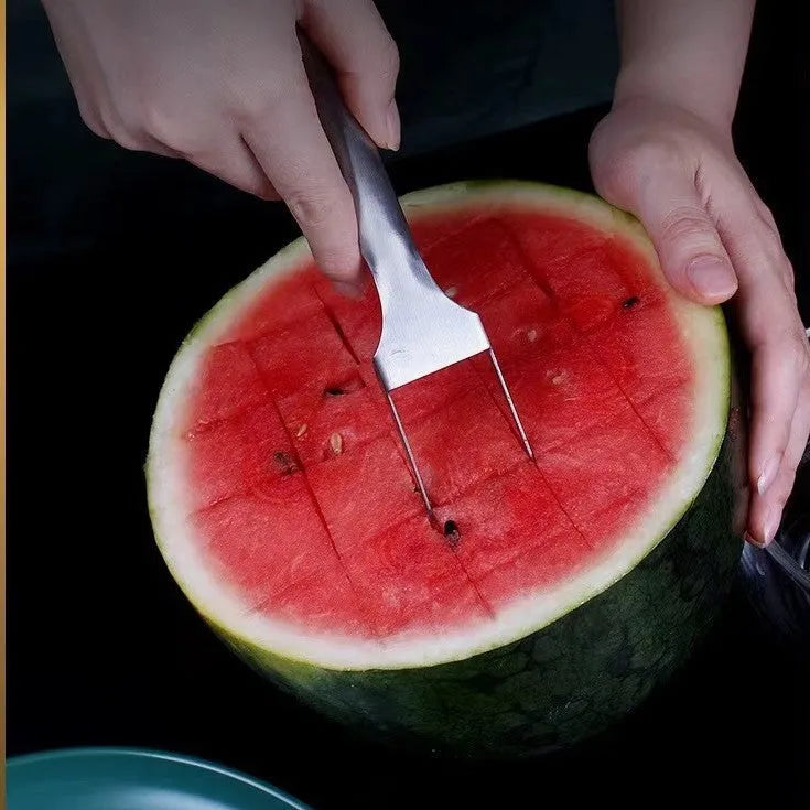 Silver stainless steel watermelon slicer and serving fork with a long handle on a kitchen surface