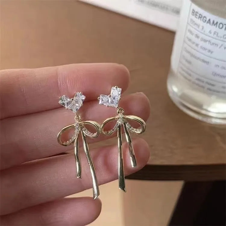 Pair of alloy bow tie ear studs with love heart zircon centre on light background