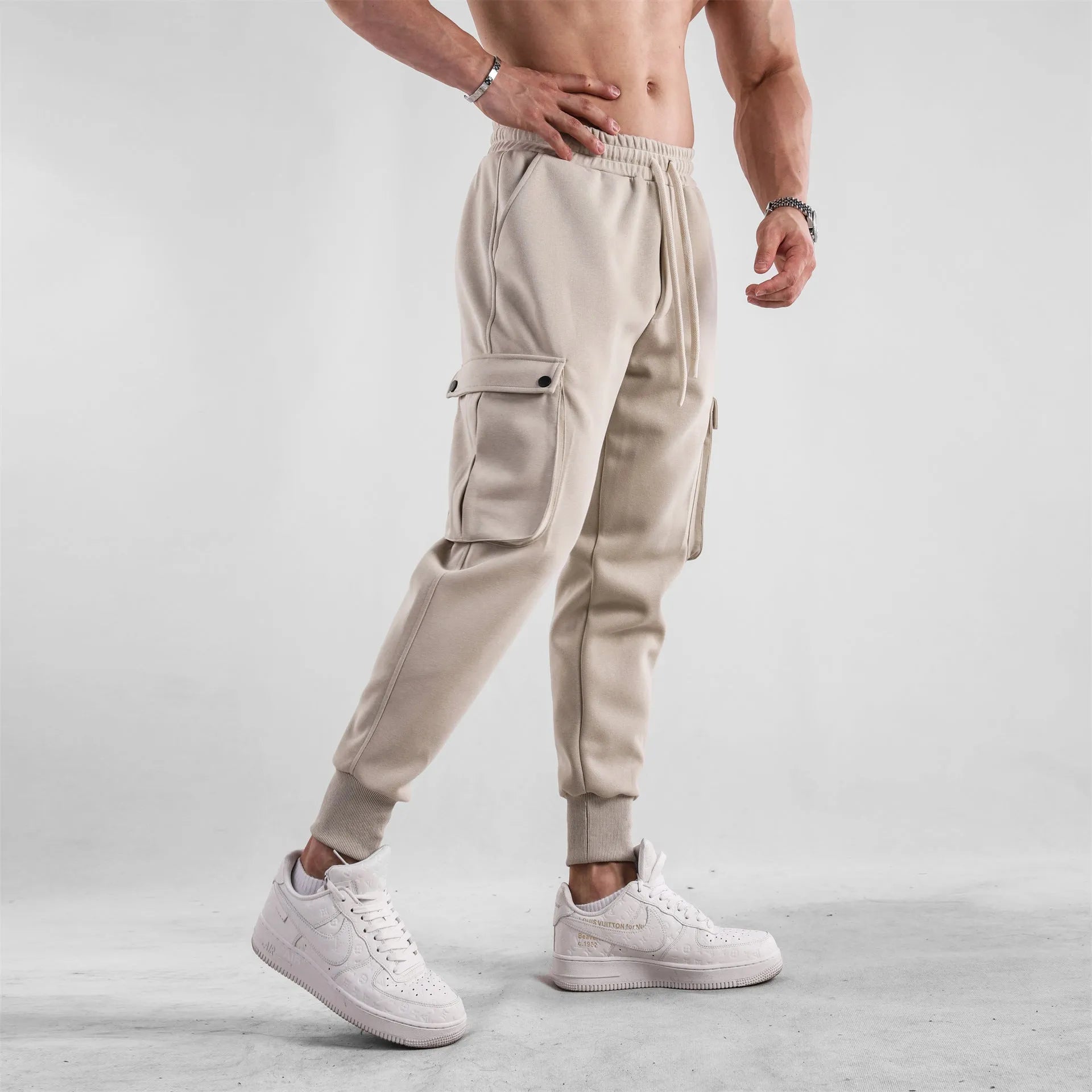 Men's loose beige cotton trousers with an ankle tie and multiple pockets on a casual model.