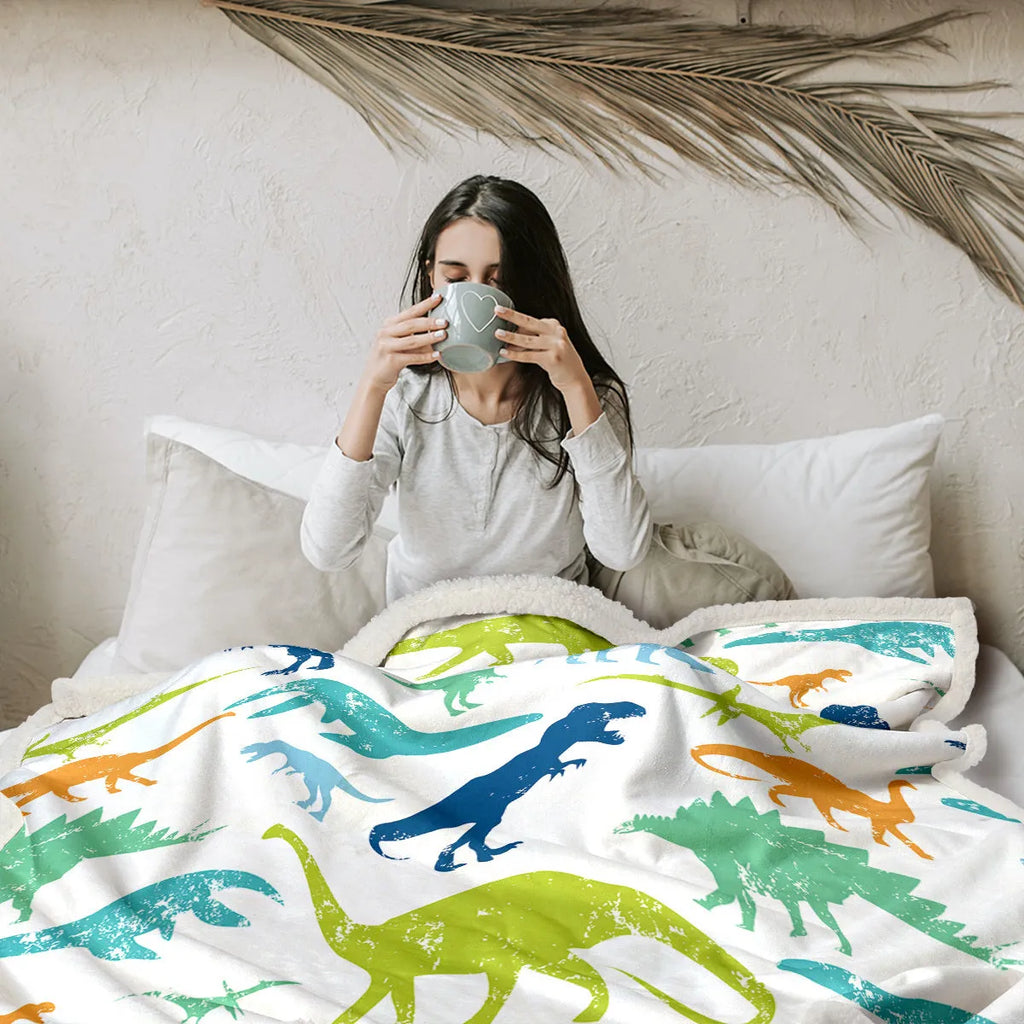 Dinosaur themed white sherpa fleece lamb wool blanket folded on a sofa