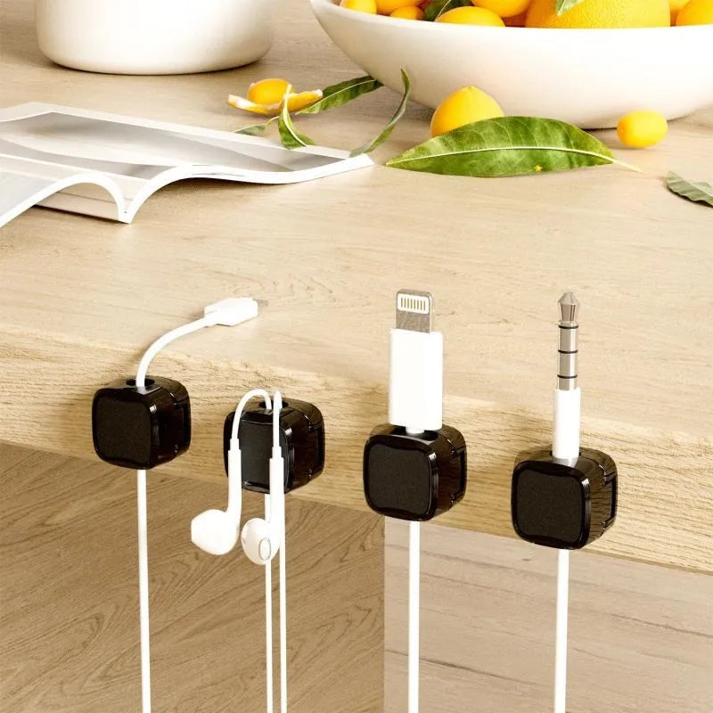 White and black magnetic cable clips holding a USB cable against a wooden desk edge.