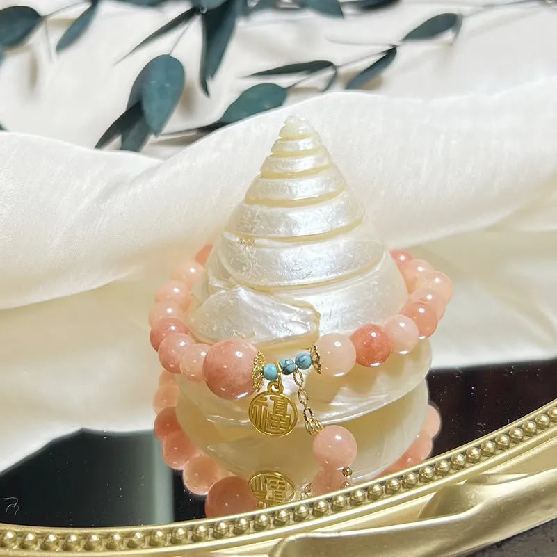 Close-up of a women's pink natural stone and alloy charm bracelet on a wrist, showing adjustable fastening.