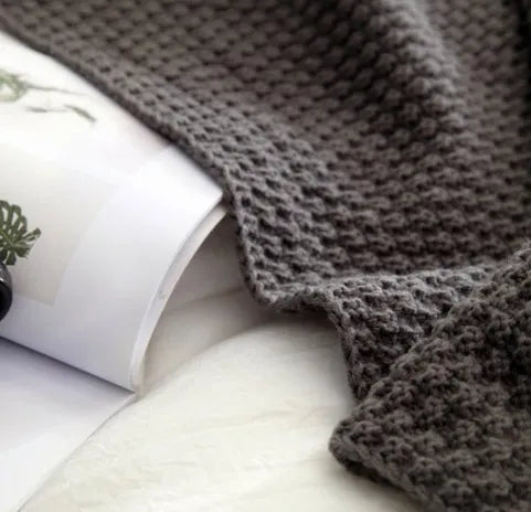 Nordic style fringed knit ball acrylic throw blanket in beige colour on a sofa.