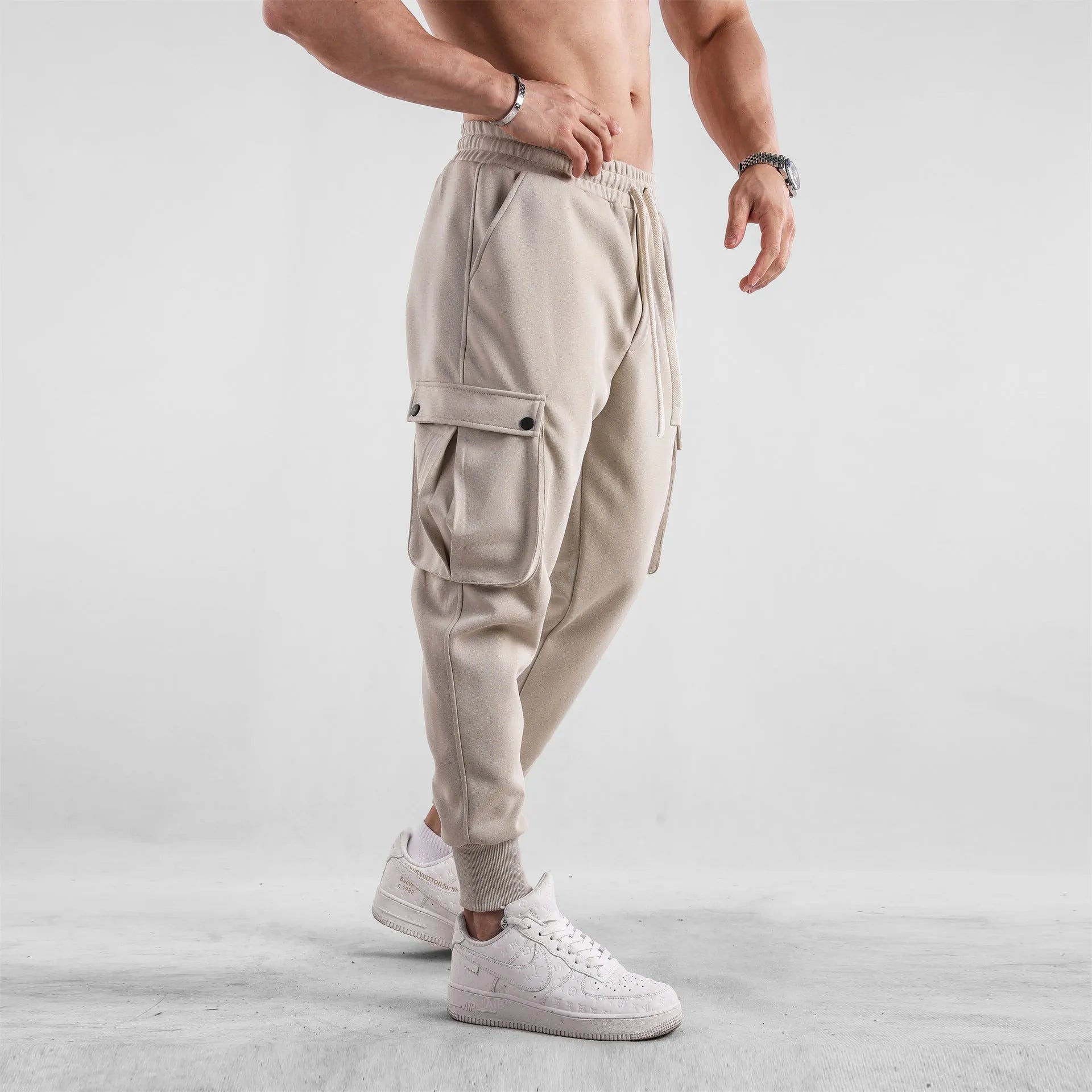 Men's loose beige cotton trousers with an ankle tie and multiple pockets on a casual model.