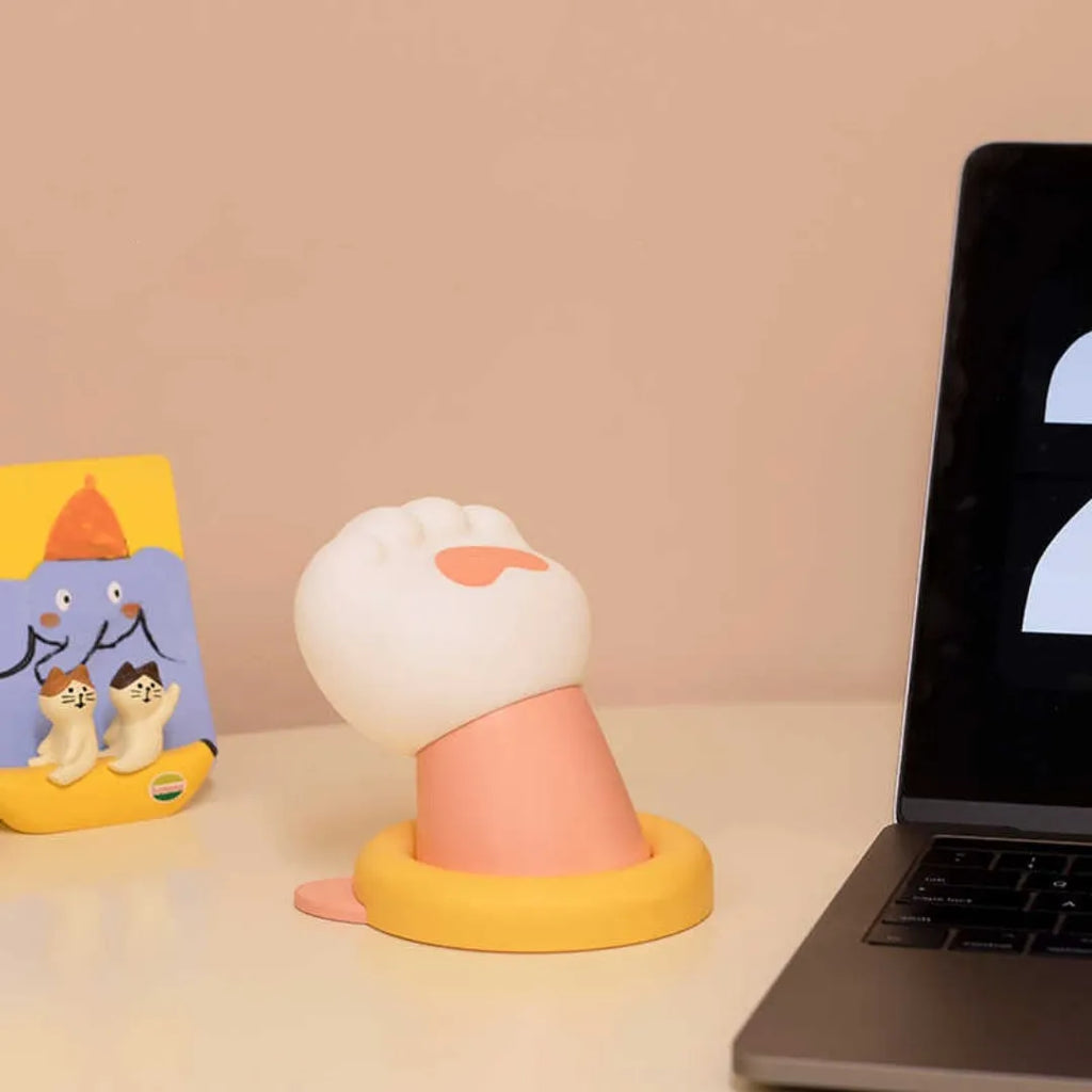 White rechargeable cat paw touch lamp with adhesive back, lit on a bedside table.