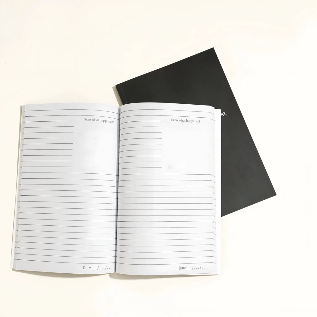 Black hardcover dream journal notebook with plain paper pages open on a desk.