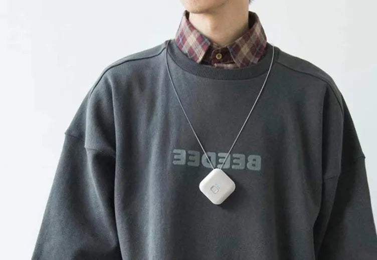 Compact pink USB portable air purifier necklace on a table with charging cable.