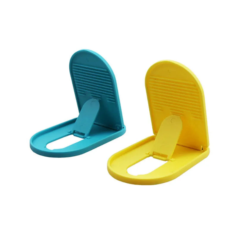 Plastic lazy bracket mobile phone stand on a desk, shown in assorted colours including black, blue, and pink.