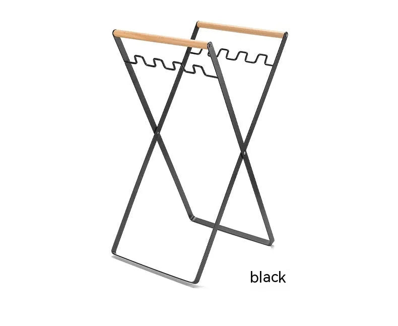 Black iron folding bin rack with wooden handles holding two rubbish bags in an outdoor setting.