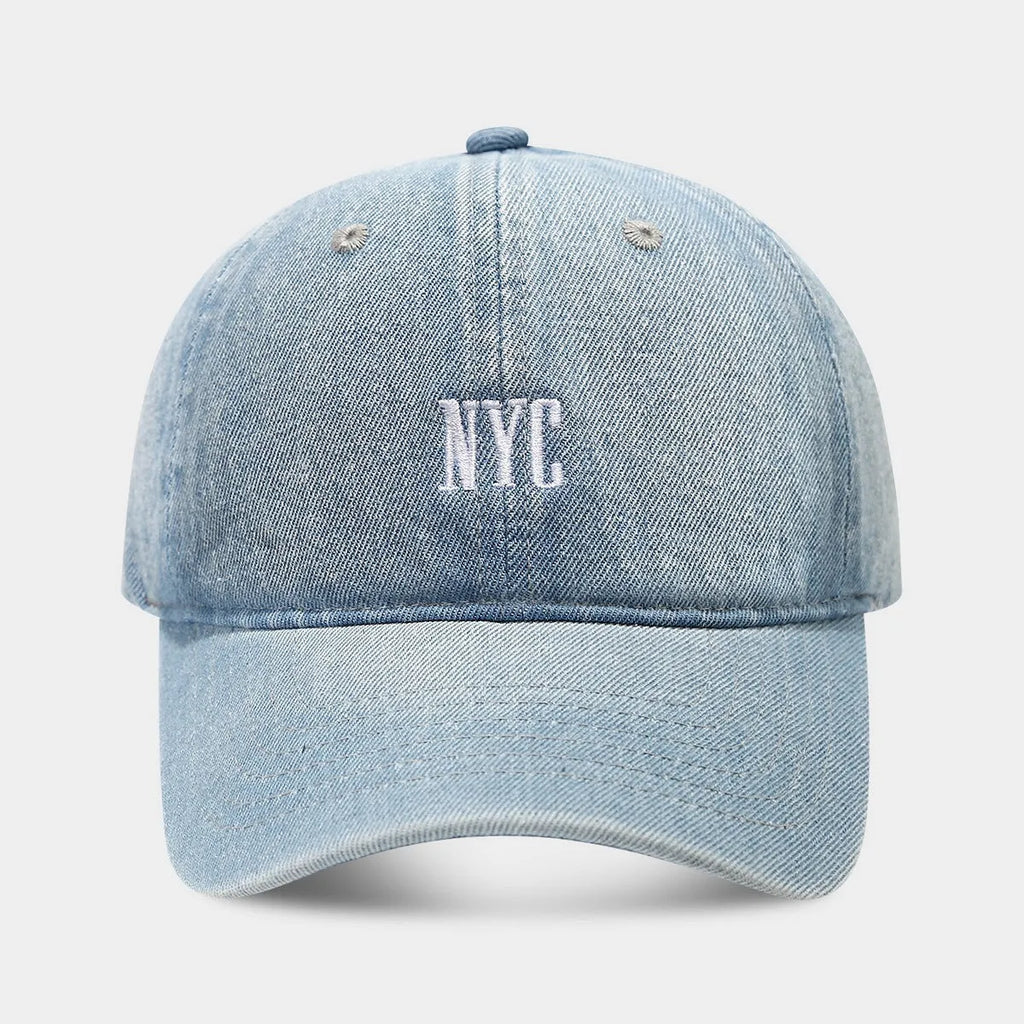 A light blue denim peaked cap with a dome crown, adjustable strap, and decorative white English letters on the front.