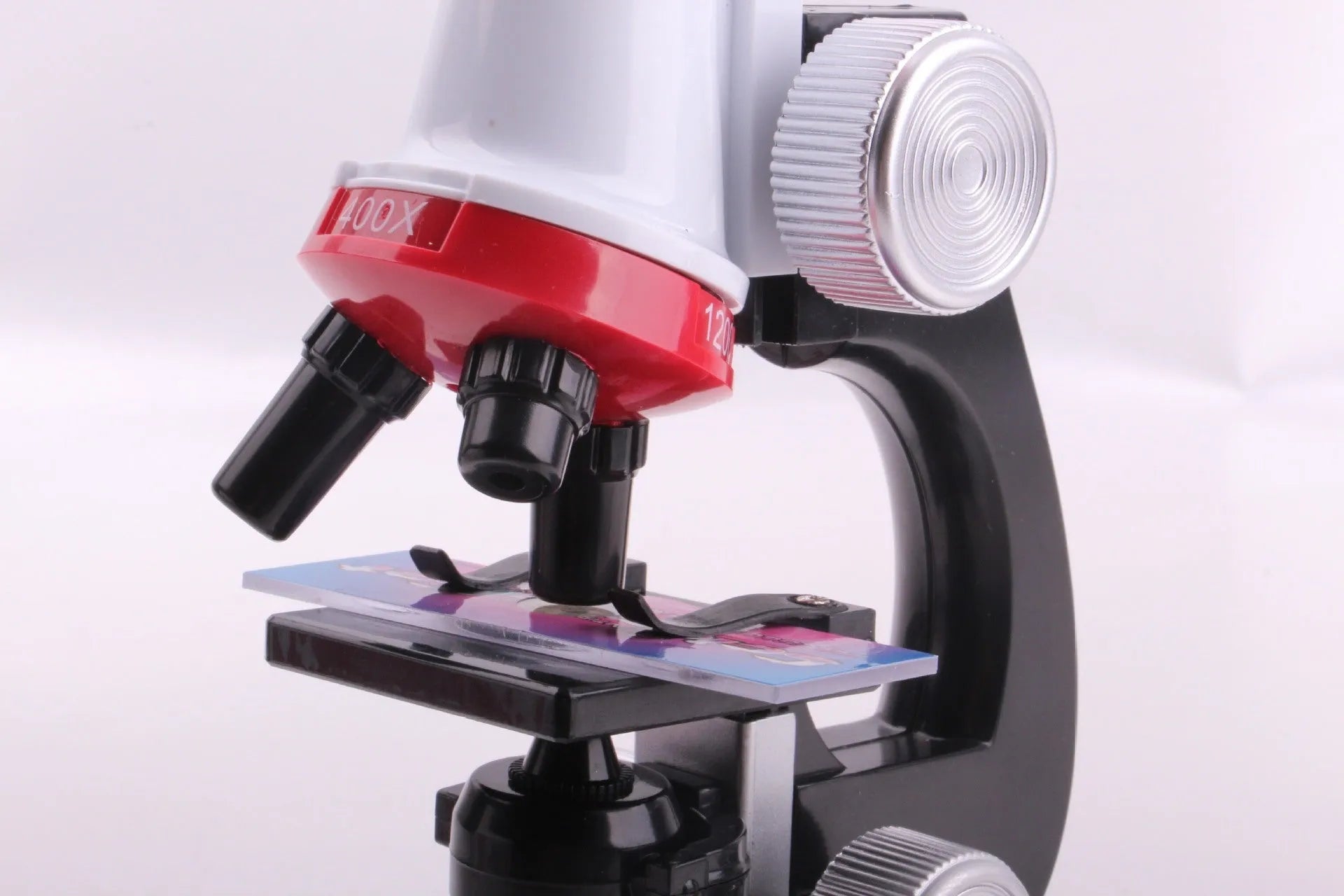 Child biological microscope with LED light, three objective lenses, and coarse focus knob on white background