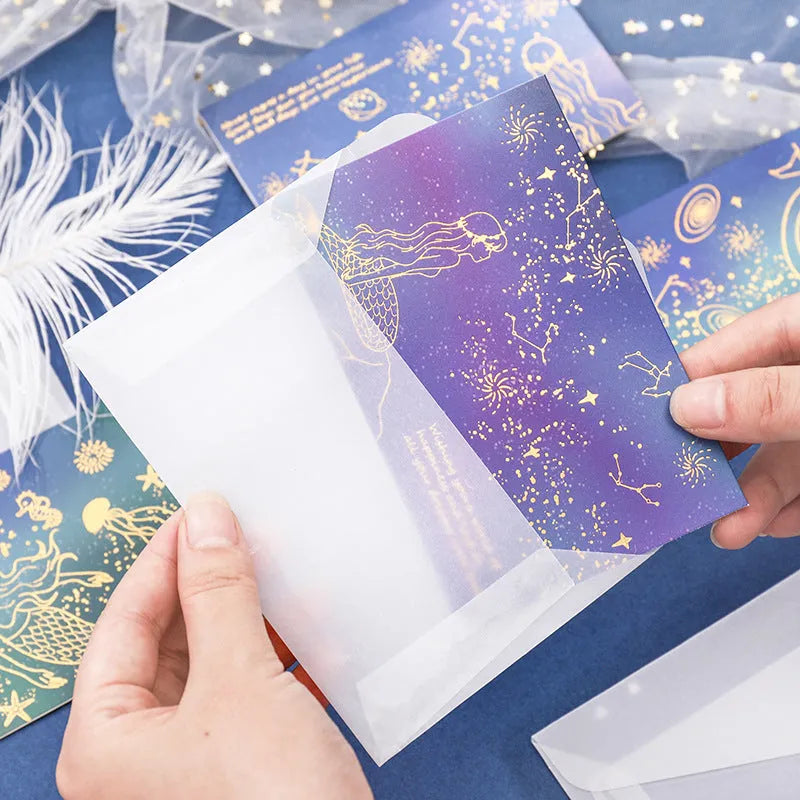 Set of three gilded greeting card envelopes in galaxy colour designs on a dark background.