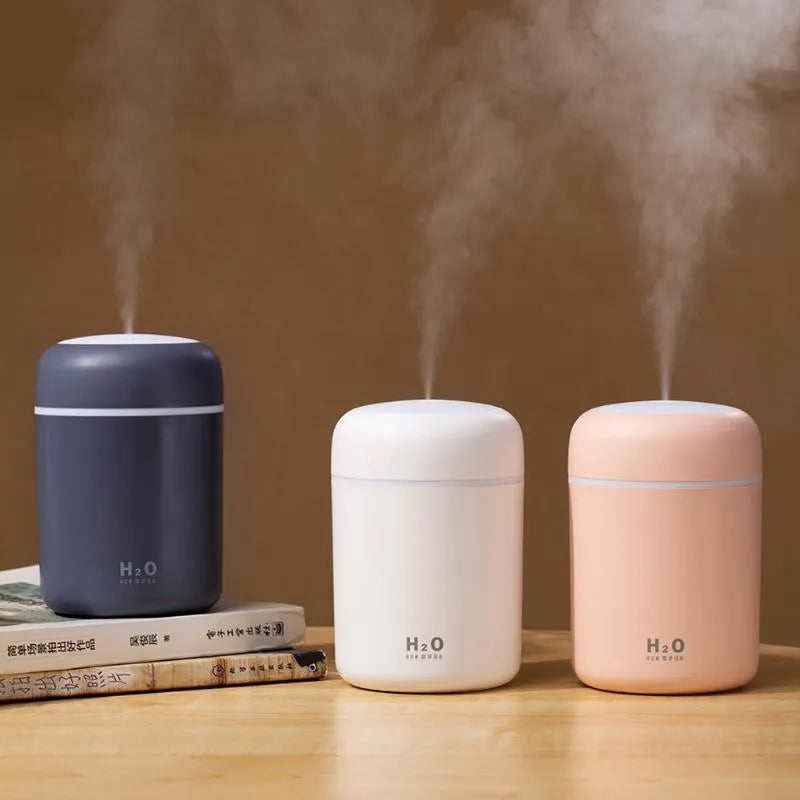 Pink, white, or navy blue USB mini desktop humidifier with atmosphere lights on a desk.
