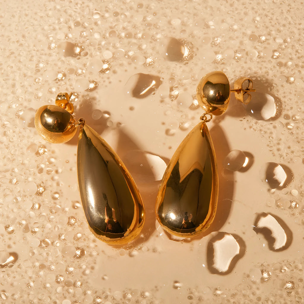 Gold coloured geometric hemisphere earrings with a dangling water drop pendant, made from stainless steel.