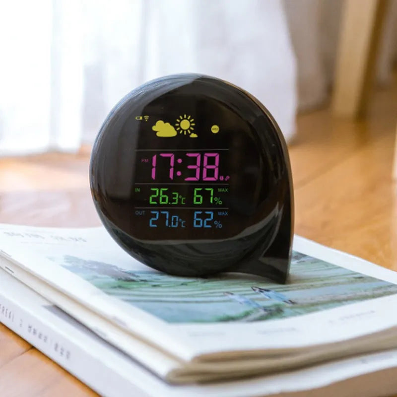 Black wireless weather forecast clock with outdoor sensor showing temperature and humidity on colour LED display