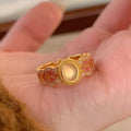 Gold geometric open ring with a pink crystal enamel stone on a model's finger.
