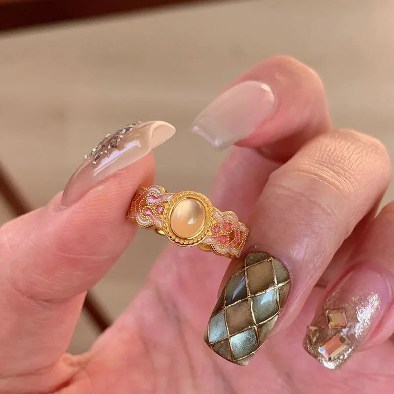Gold geometric open ring with a pink crystal enamel stone on a model's finger.