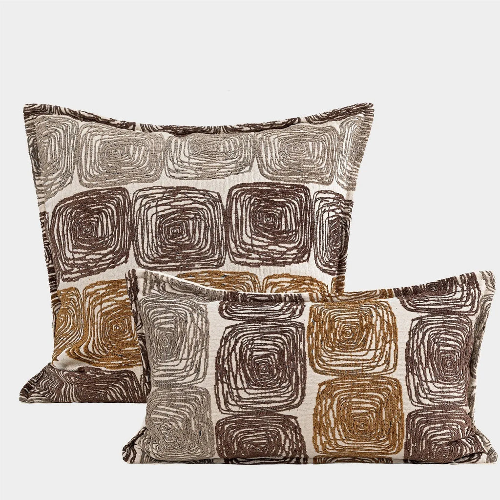 Cream and coffee coloured abstract coil pattern square pillow cover on a grey sofa.