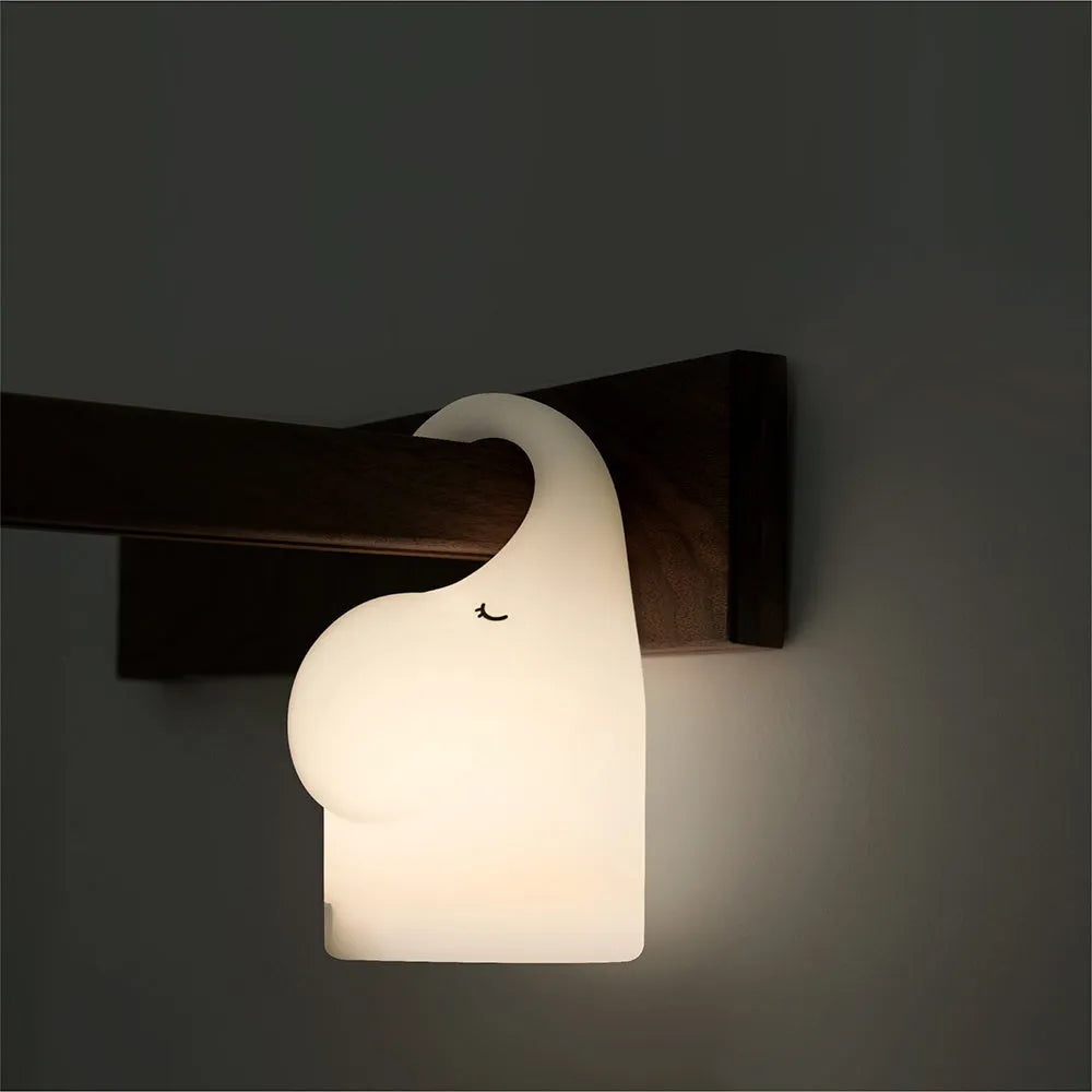 White silicone elephant-shaped night light with a warm glow, placed on a wooden bedside table.