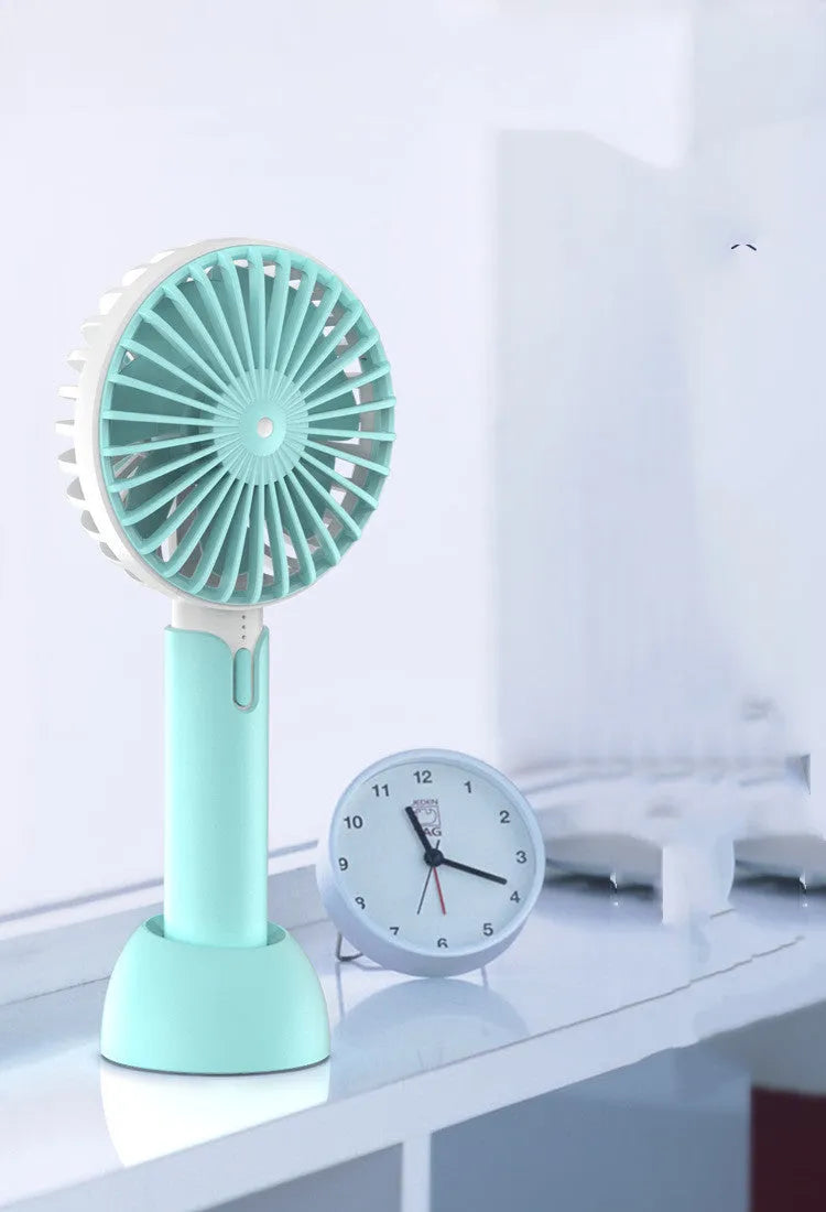 Blue handheld USB mini electric fan with three-speed control on a desk.
