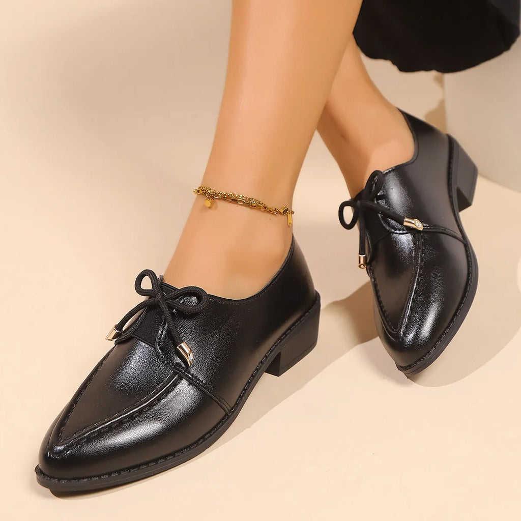 Women's black leather-look flat shoes with a decorative bow on the pointed toe.