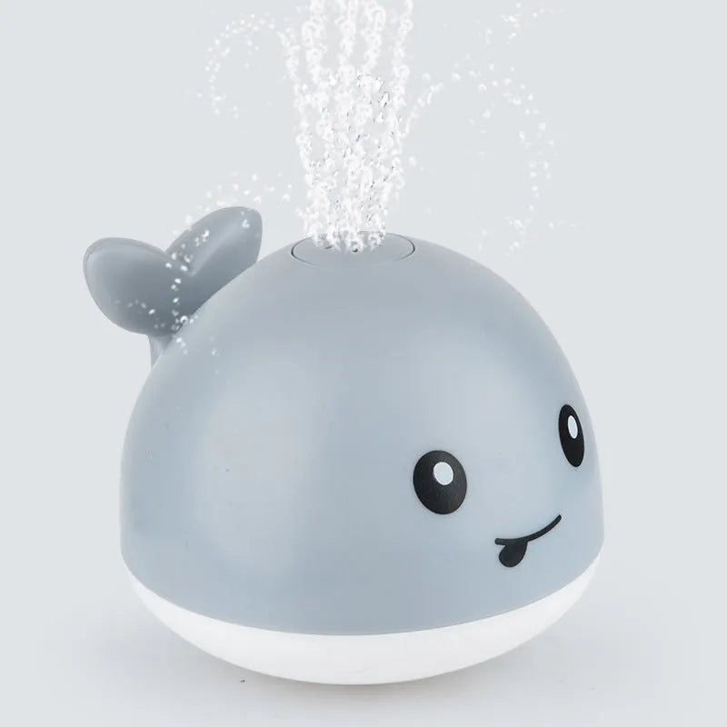 Whale-shaped electric bath toy spraying water with flashing lights, floating in baby bathtub