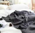Nordic style fringed knit ball acrylic throw blanket in beige colour on a sofa.