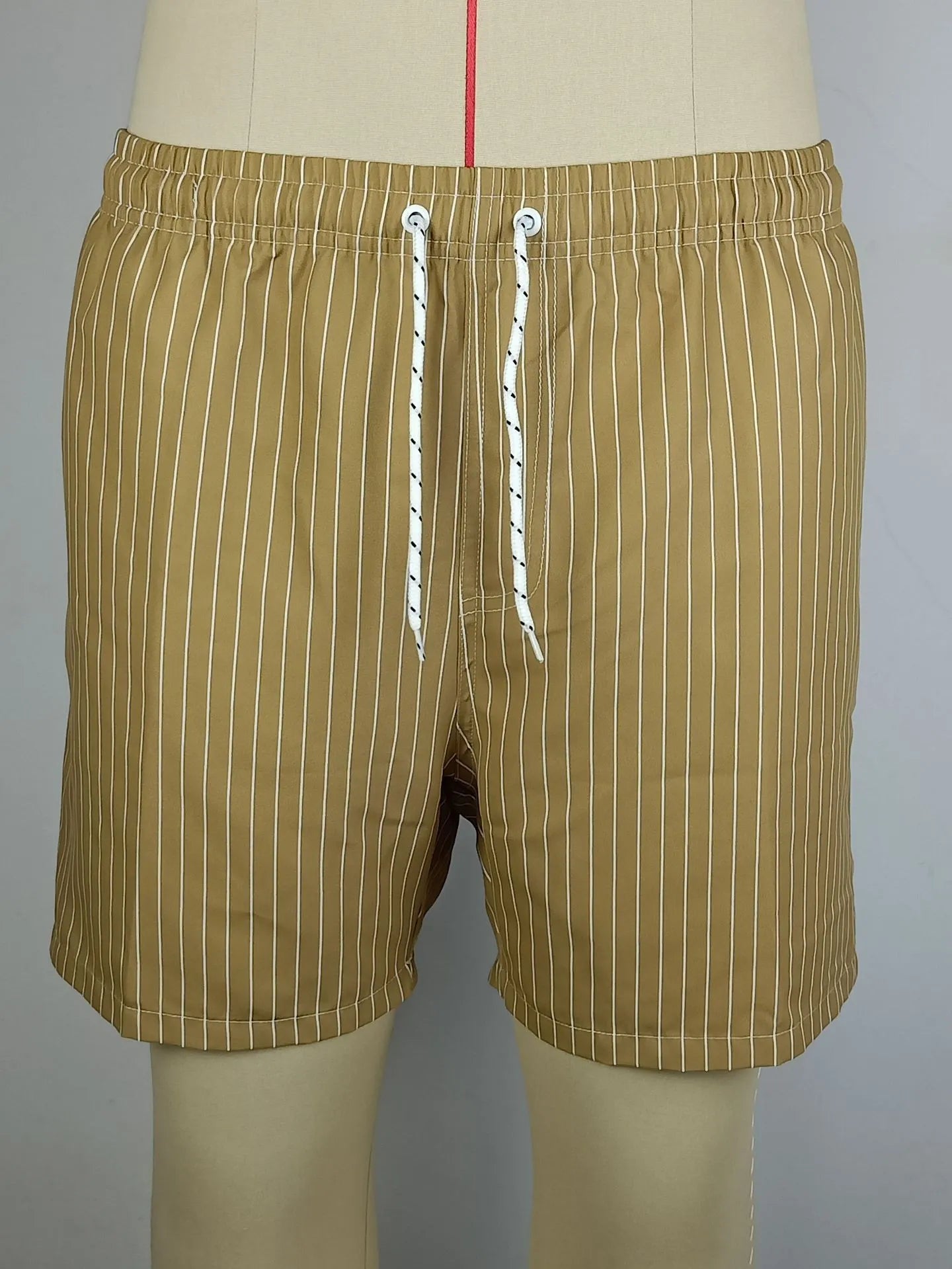 Man wearing navy blue and white striped straight-leg polyester beach shorts on shore.