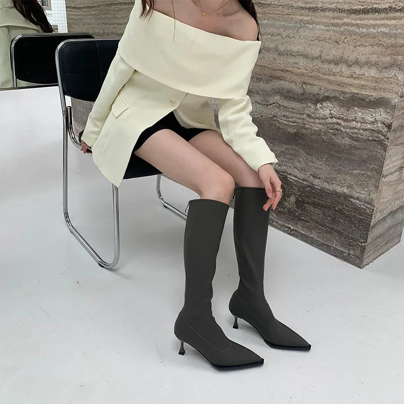 Women's black pointed toe stiletto heel boots with a back zipper, showing the below-the-knee shaft.