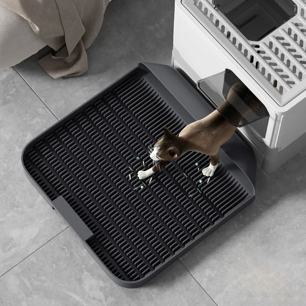 Large black cat litter pedal with slanted mouth and textured non-slip mat next to litter tray