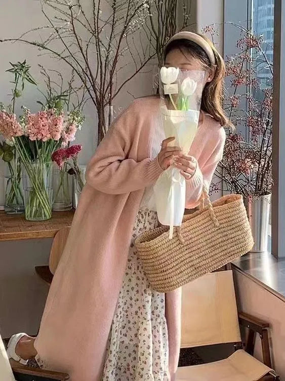 A woman wearing a khaki, mid-length, knitted V-neck cardigan with long sleeves.
