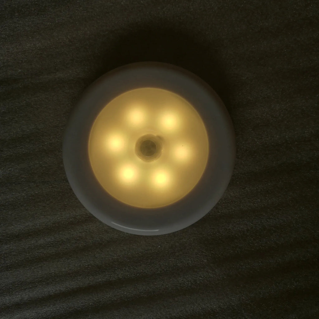 6LED motion sensor nightlight with strong magnet, white body, mounted on a ceiling corner, with motion detection arrows shown