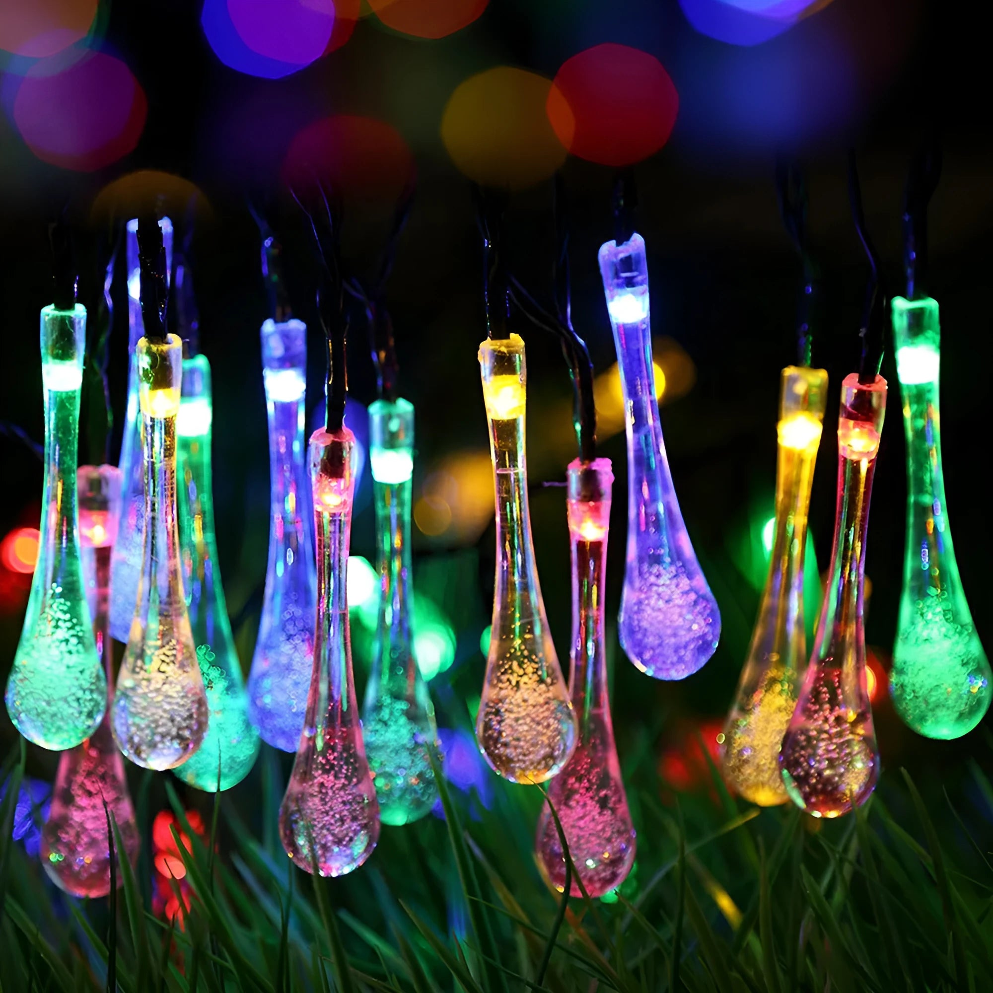 Water drop shaped solar LED fairy lights hanging outdoors with solar panel and ground spike.