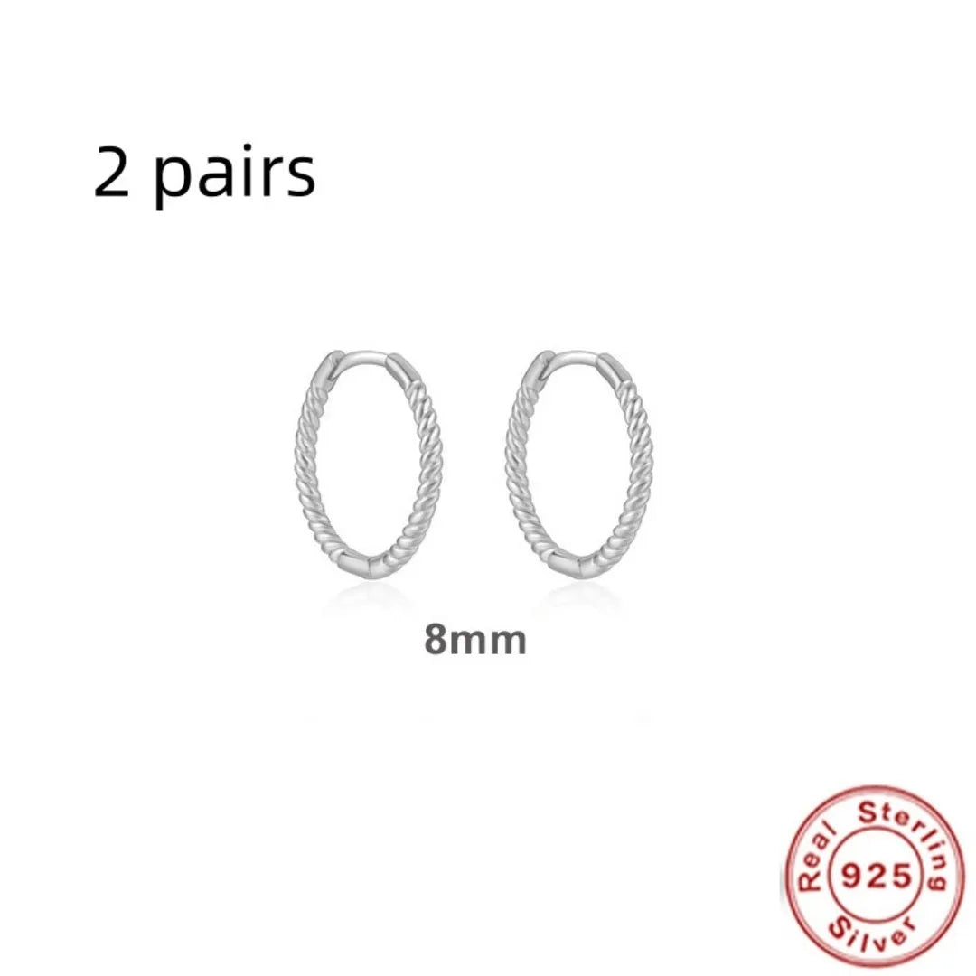 Close-up of twisted S925 sterling silver round ring earrings in gold colour on a plain background.