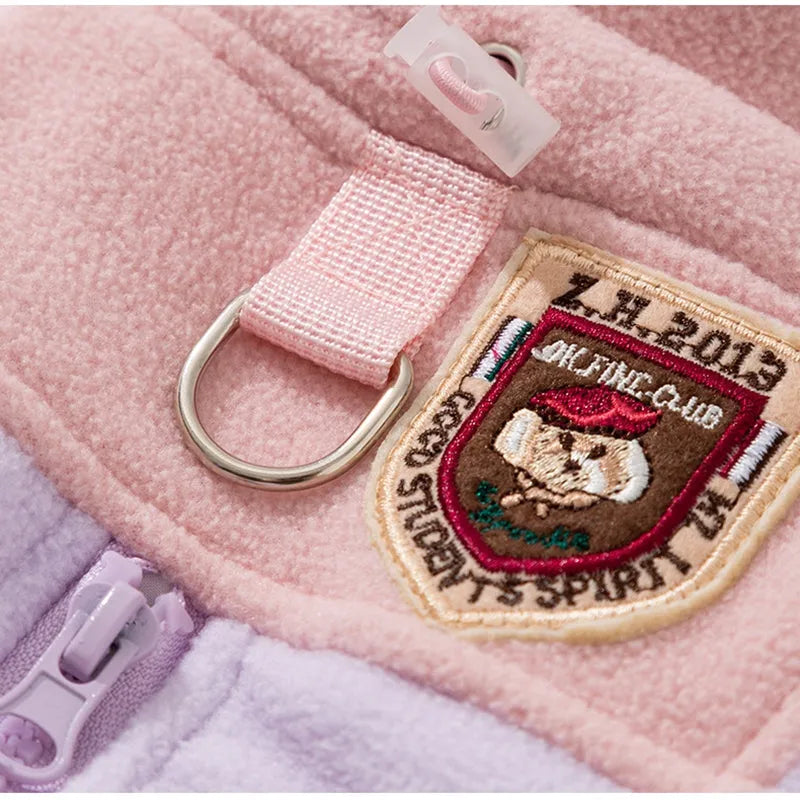 Small dog wearing a colour-block fleece jumpsuit in purple and pink, with full-zip front and leash ring