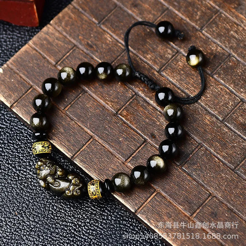 Close-up of a black obsidian bead bracelet with a detailed silver Pi Xiu charm on a neutral background.