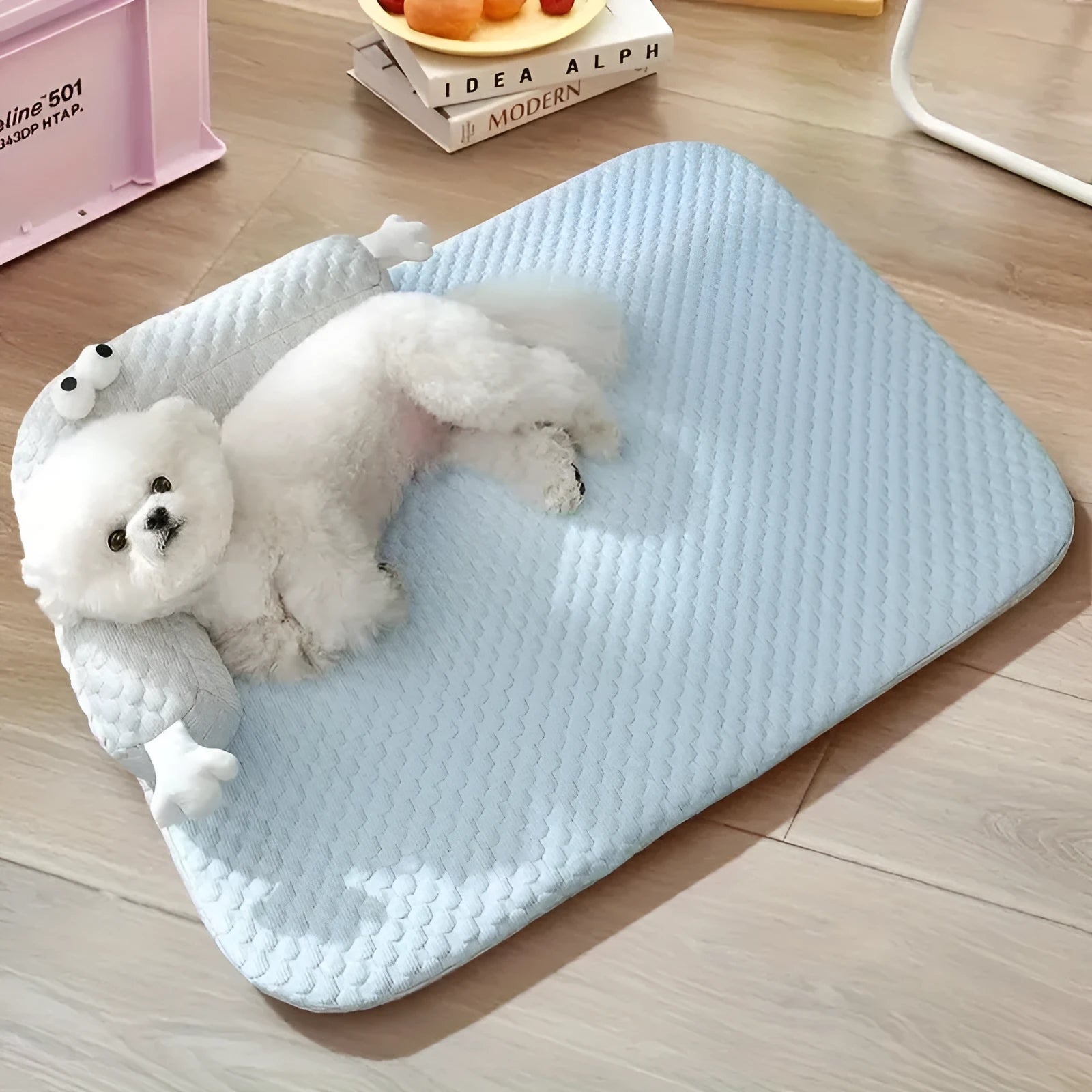 Blue pet cooling pad with big-eyed monster design, shown on a wooden floor.