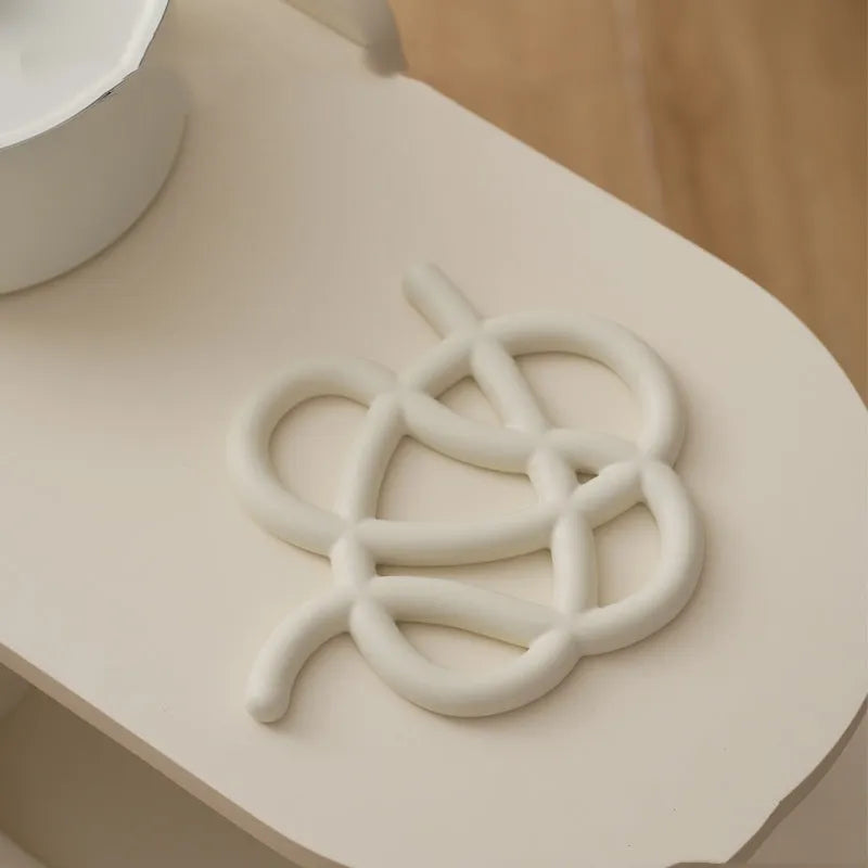 Ceramic heat proof mat in irregular shape on a table, shown in bright black colour.