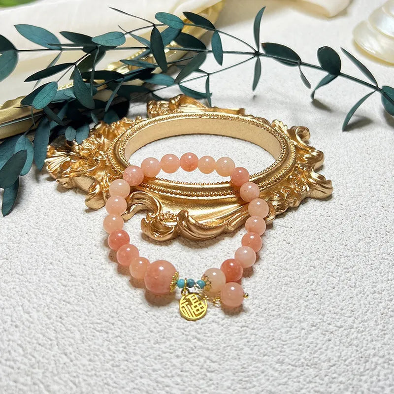 Close-up of a women's pink natural stone and alloy charm bracelet on a wrist, showing adjustable fastening.